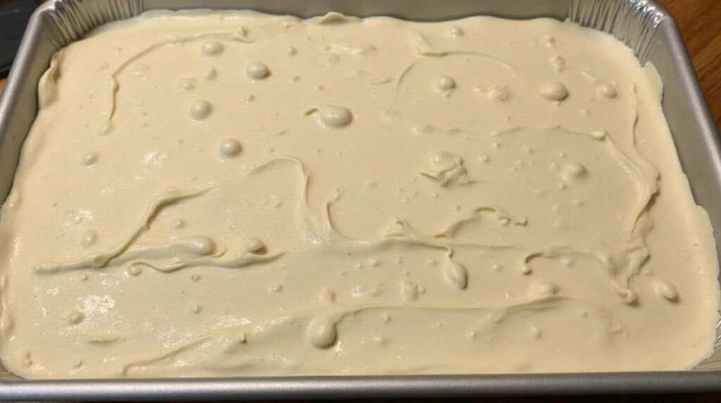 Unbaked kefir sheet cake batter in a rectangular metal baking pan, smooth and ready for the oven.